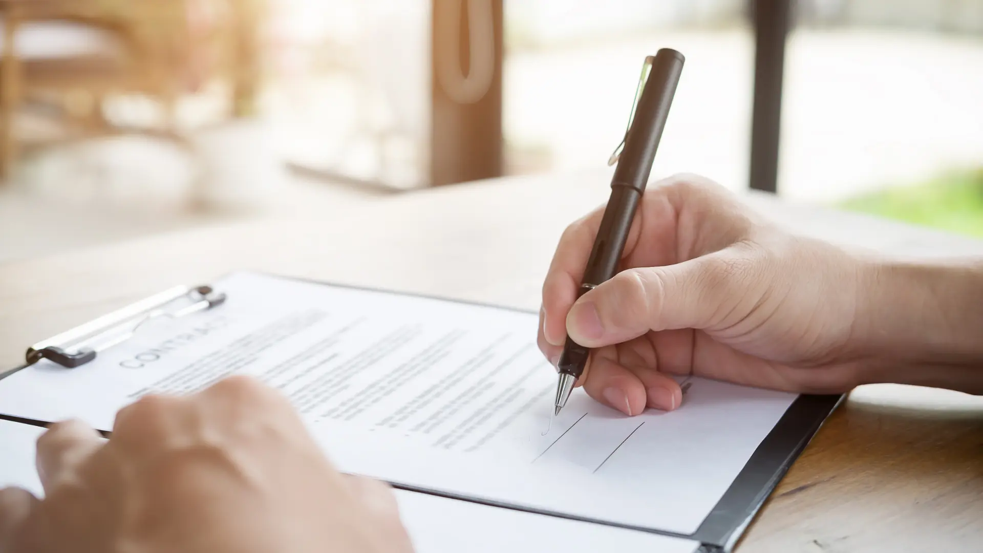 Light skin tone hands holding a pen and signing a contract