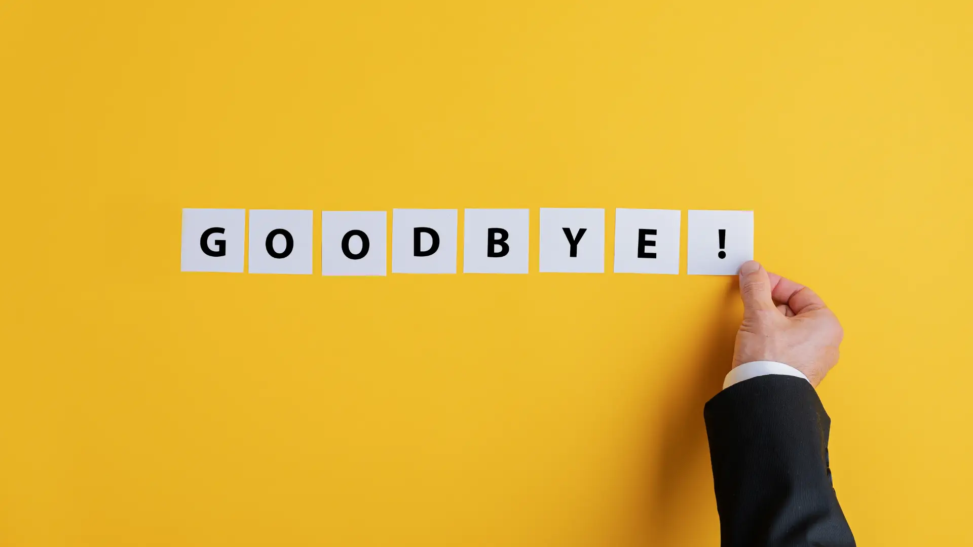 A man resigning from job; he is sticking the words "Goodbye!" onto a yellow wall.